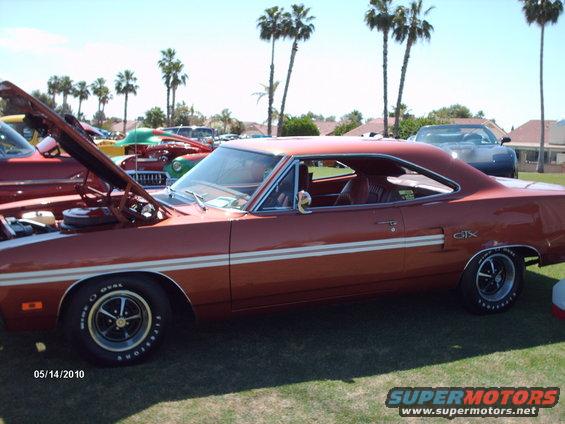 Orange muscle car with white side stripes and a GTX badge, parked on grass
