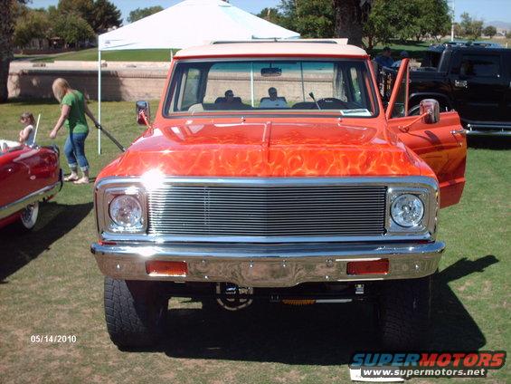Front view of an orange pickup truck with flame graphics. Door is open. Another car is to the left