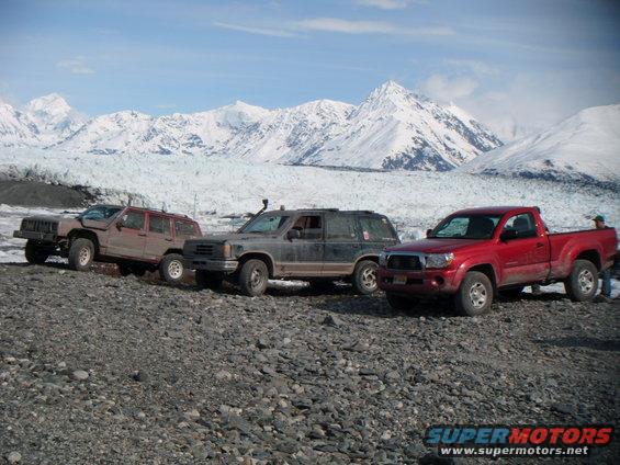 1998 Jeep Cherokee parked with two other SUVs and a red pickup truck in front of a glacier and mountains