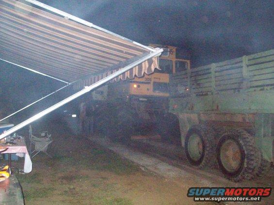 Yellow truck cab with number 309 and a green trailer with wooden sides, parked outdoors at night under an awning