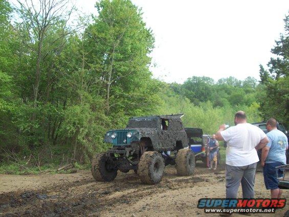 Mud-covered Jeep Wrangler with oversized tires on a dirt track