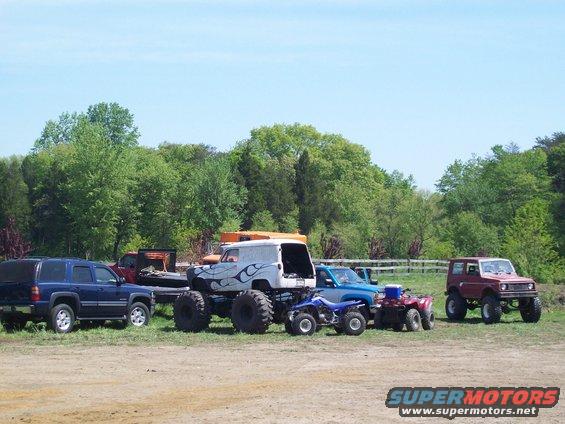 Several off-road vehicles and ATVs parked in a grassy area with trees in the background
