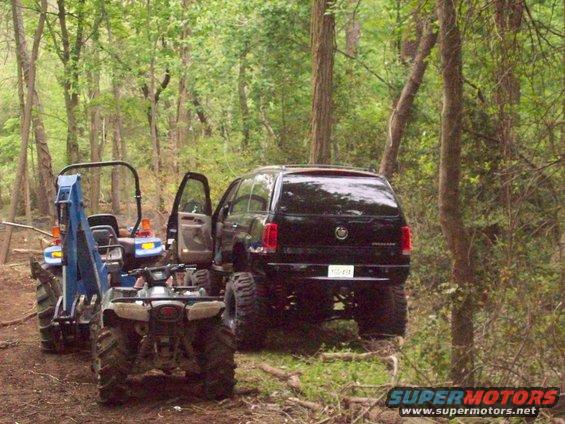 Lifted black Cadillac Escalade parked off-road with a tractor and ATV