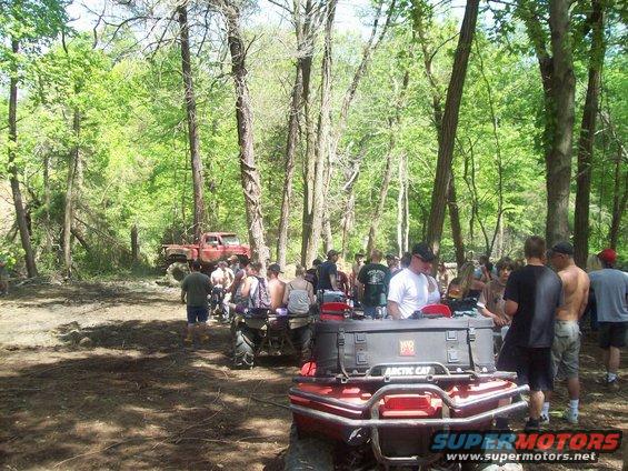Group of people gathered in a wooded area with ATVs and a red pickup truck
