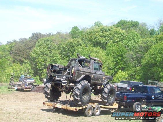 Monster truck with large tires on a trailer, a blue pickup truck is behind it
