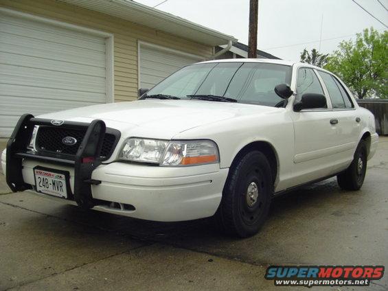 White Ford Crown Victoria police car with a push bumper parked in front of a garage