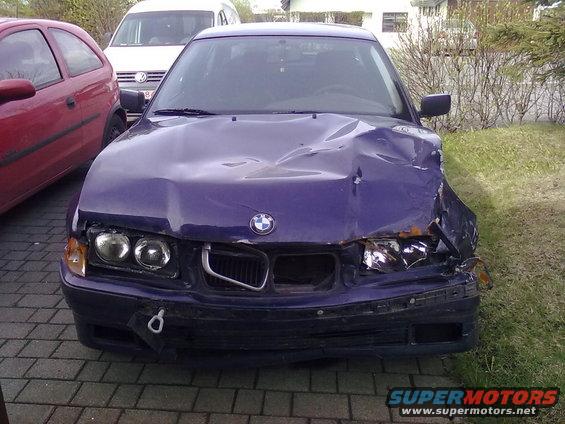 Front view of a damaged purple 1998 BMW 3 Series with a red car and white van in the background