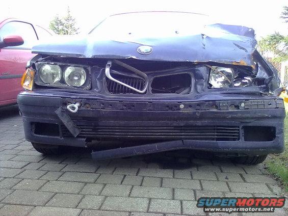Front of a dark blue 1998 BMW 3 Series with heavy front-end damage, including a crumpled hood and broken bumper