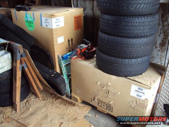 Stack of four tires on top of a large cardboard box, with other boxes and a chainsaw in the background