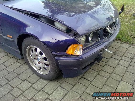 Damaged blue 1998 BMW 3 Series front end, showing dented hood, broken headlight, and torn bumper