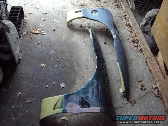 Two car fenders, one dark green and one dark blue, lying on a concrete floor with scattered leaves