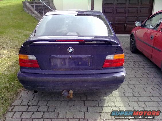 Rear view of a dark blue BMW sedan with a spoiler and a tow hitch. A red car is parked next to it