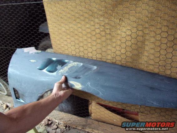 Hand holding a gray car fender with vents, showing bodywork in progress