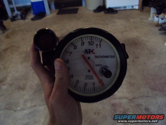 Tachometer gauge with red needle and RPM x1000 markings, held in hand