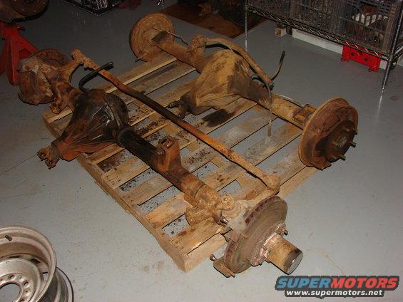 Two rusty vehicle axles with brake drums and hubs are laid out on a wooden pallet