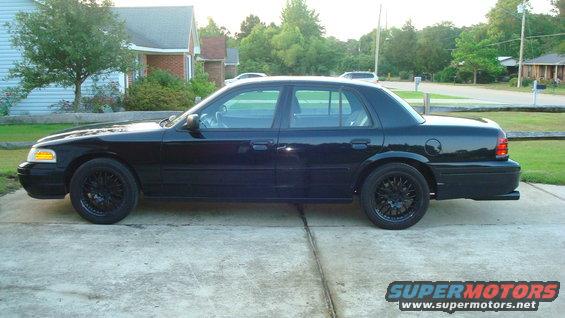 Black Ford Crown Victoria sedan, side view, black aftermarket wheels, parked in driveway