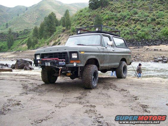 Olive green 1978 Ford Bronco with roof rack parked on a sandy riverbank