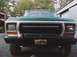 1979 Ford Bronco - Front view of a green truck, possibly a 1979 Ford Bronco, a prominent black grille and bumper with a decorative license plate.