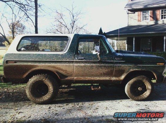 Mud-covered green and white 1978 Ford Bronco, side view, parked on gravel near a house