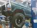 1979 Ford Bronco - A green Ford pickup truck is raised on a hydraulic lift in a garage, revealing its undercarriage and large tires.
