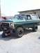 1979 Ford Bronco - A person works on the underside of a green 1979 Ford Bronco with a white removable top and large off-road tires.