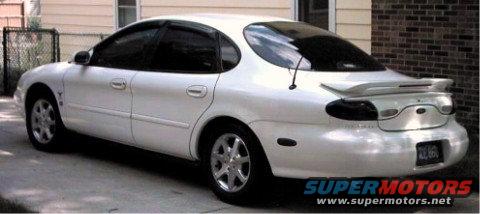 White sedan parked in driveway, rear view. Spoiler on trunk, tinted windows, aftermarket wheels