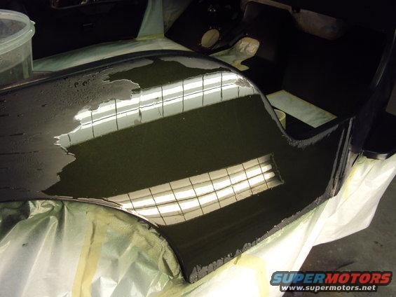 Dark car part covered in liquid, resting on drop cloths