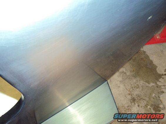 Brushed metal panel with a curved cutout and a sharp corner, resting on a concrete floor