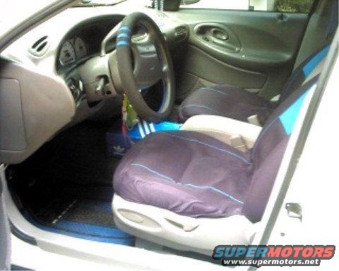 1997 Ford Taurus interior, driver's side view. Gray dashboard, blue and black seat covers, floor mats