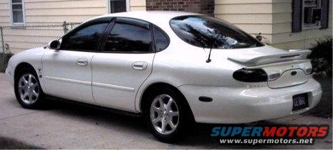 White sedan parked on concrete driveway, rear quarter view. Tinted windows, spoiler, and aftermarket wheels