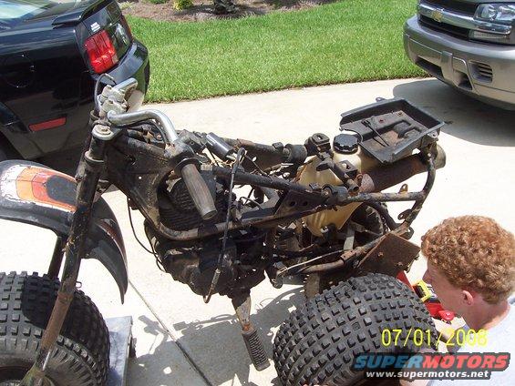 Disassembled three-wheeled ATV frame with engine and tires removed. A person is looking at the parts