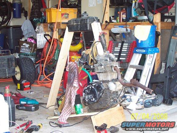 Engine and gas tank on floor, surrounded by tools, ladder, and other garage items