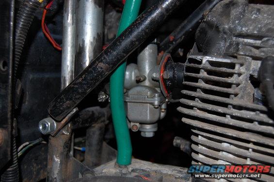 Close-up of a motorcycle's carburetor and part of the engine block. Green fuel line visible