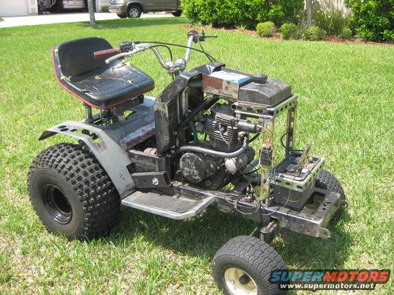 Modified riding mower with exposed engine and battery, parked on grass