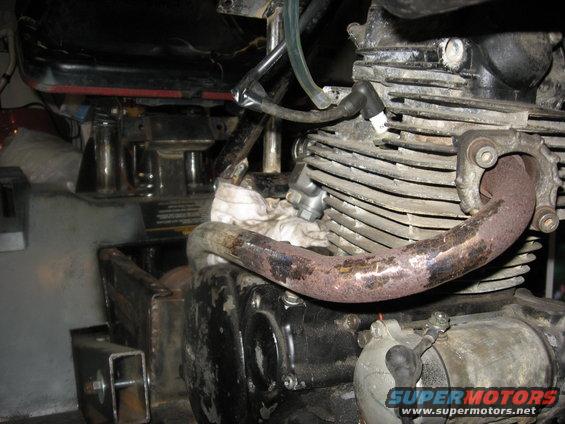 Motorcycle engine with rusty exhaust pipe and visible SuperMotors.net logo