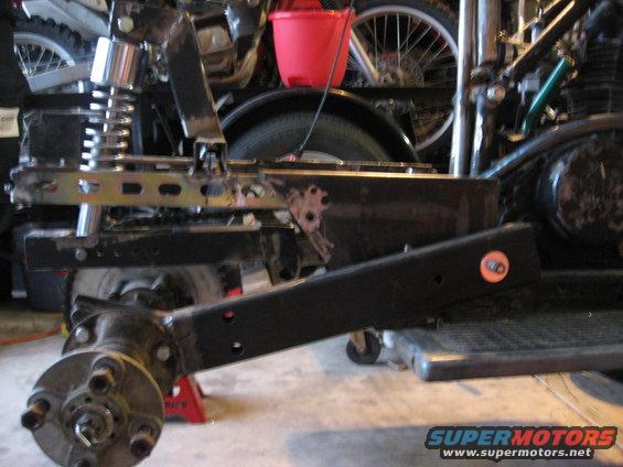 ATV frame with suspension and rear axle assembly on jack stands. Red bucket and bicycle wheels in background