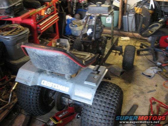 Three-wheeled riding mower in a garage with a Craftsman logo on the fender