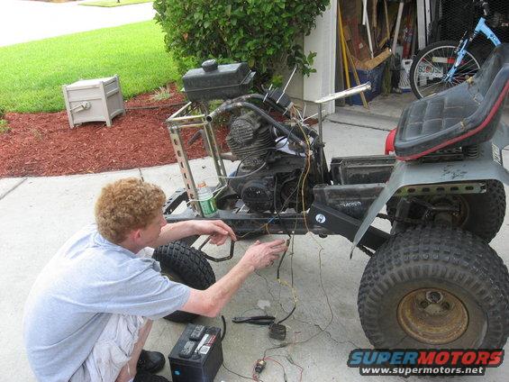 Lawn tractor frame with engine and wiring, a person works on the electrical system