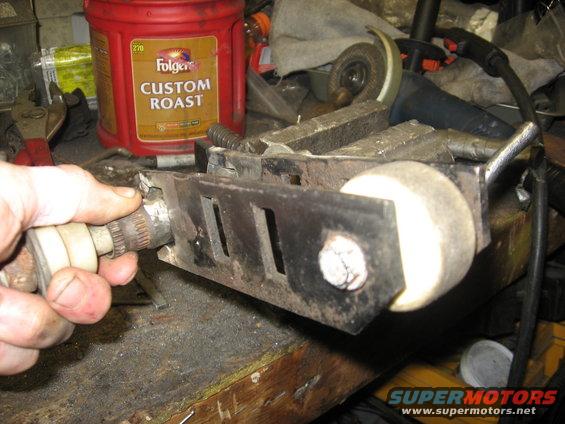 Hand holding splined shaft connected to metal bracket with roller wheel in vise