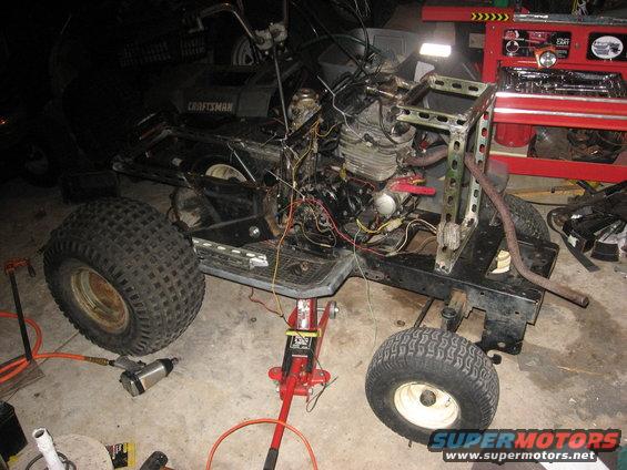 All-terrain vehicle chassis on red jack, with engine exposed, large rear tires, and metal frame