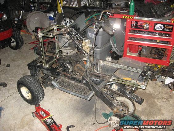 Go-kart frame with engine, carburetor, and handlebars, in a garage with tools