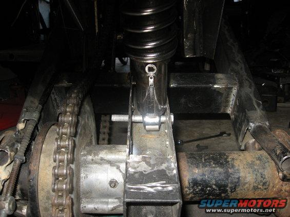 Close-up of ATV rear axle, chain, and shock absorber assembly. Some metal fabrication is visible