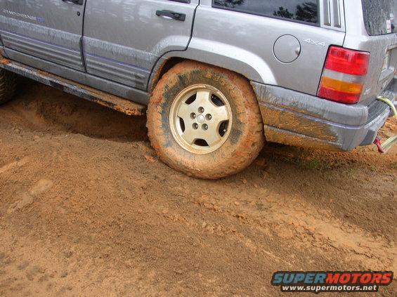 Silver Jeep Grand Cherokee with mud-covered tires stuck in dirt