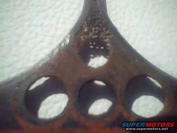 Rusty metal grille emblem with three circular cutouts and visible text