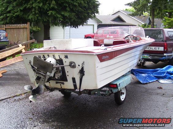 White and red boat named HAZEL M on a trailer, parked next to a red pickup truck