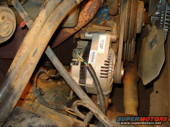 Close-up of an alternator with wires and pulleys in an engine bay. Some text is visible on a sticker on the alternator