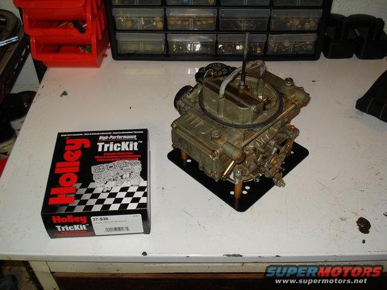 Holley TrickKit box next to a brass carburetor on a black mounting plate