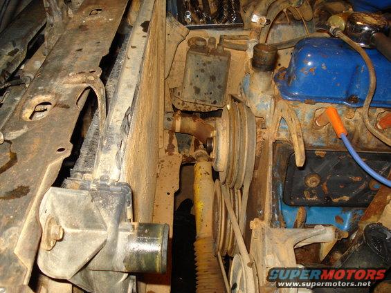 Close-up of engine bay parts including radiator, belts, pulleys, and blue valve covers
