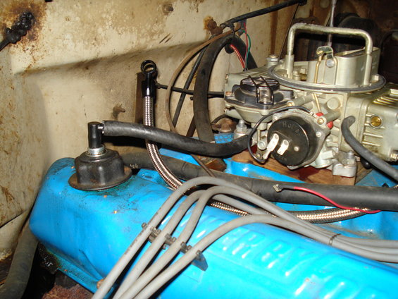 Close-up of a blue engine valve cover and a carburetor with fuel lines and spark plug wires