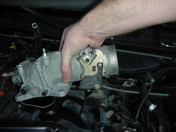 Hand holding a Ford throttle body and intake manifold assembly over a car engine